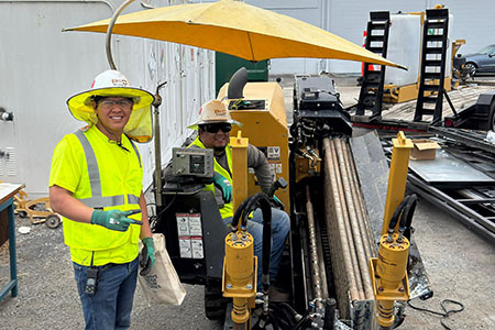 Manuel Aleon poses with an HDD crew member while he operates a Vermeer directional drill
