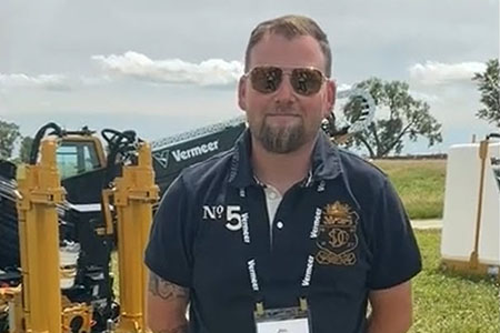 Jon Preston stands in front of a Vermeer utility drill and mixing system in a field